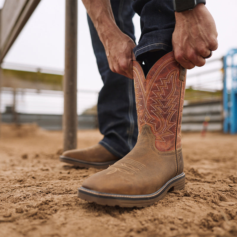Man pulling on Durango men's work boots on dirt.