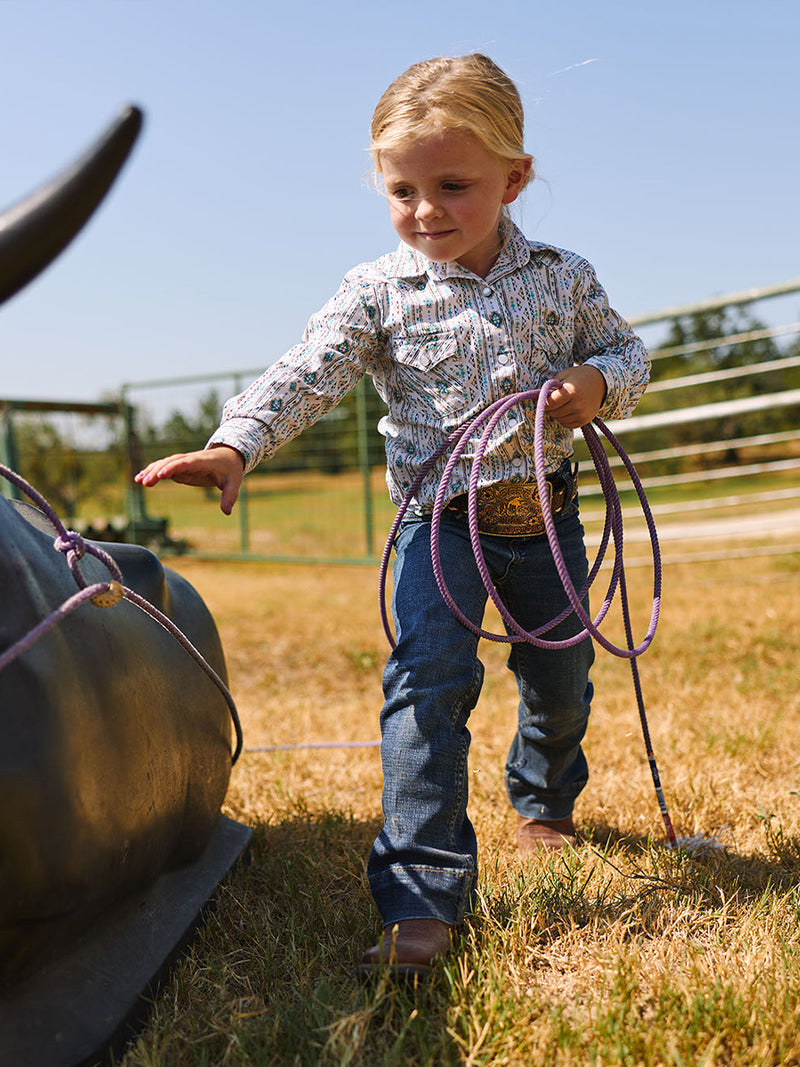 Child holding a lasso in a grassy field with a clear sky in western boots