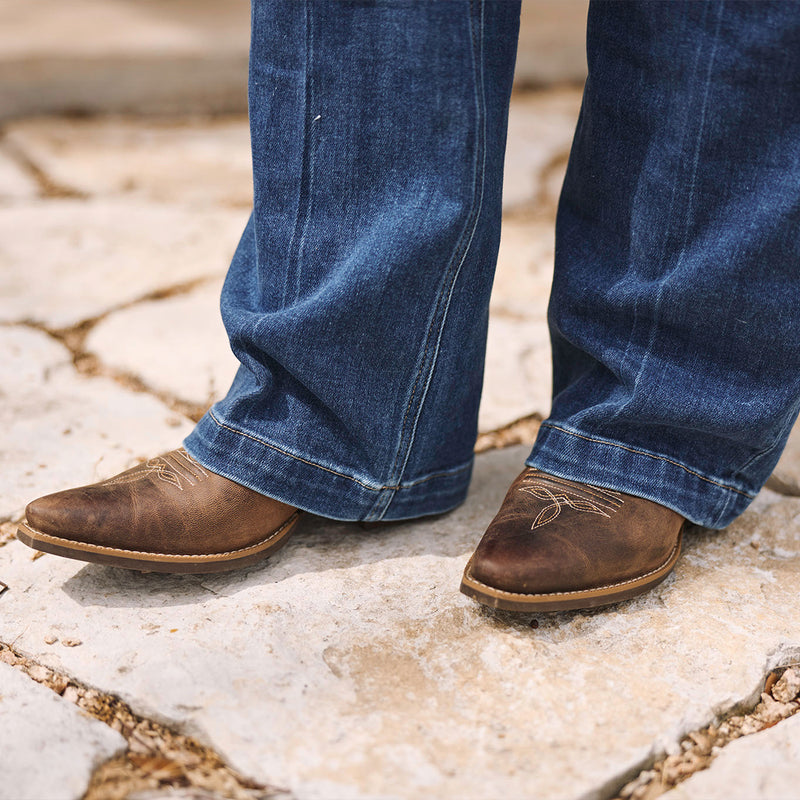 Close-up of brown Durango cowgirl boots and blue jeans on a stone pavement