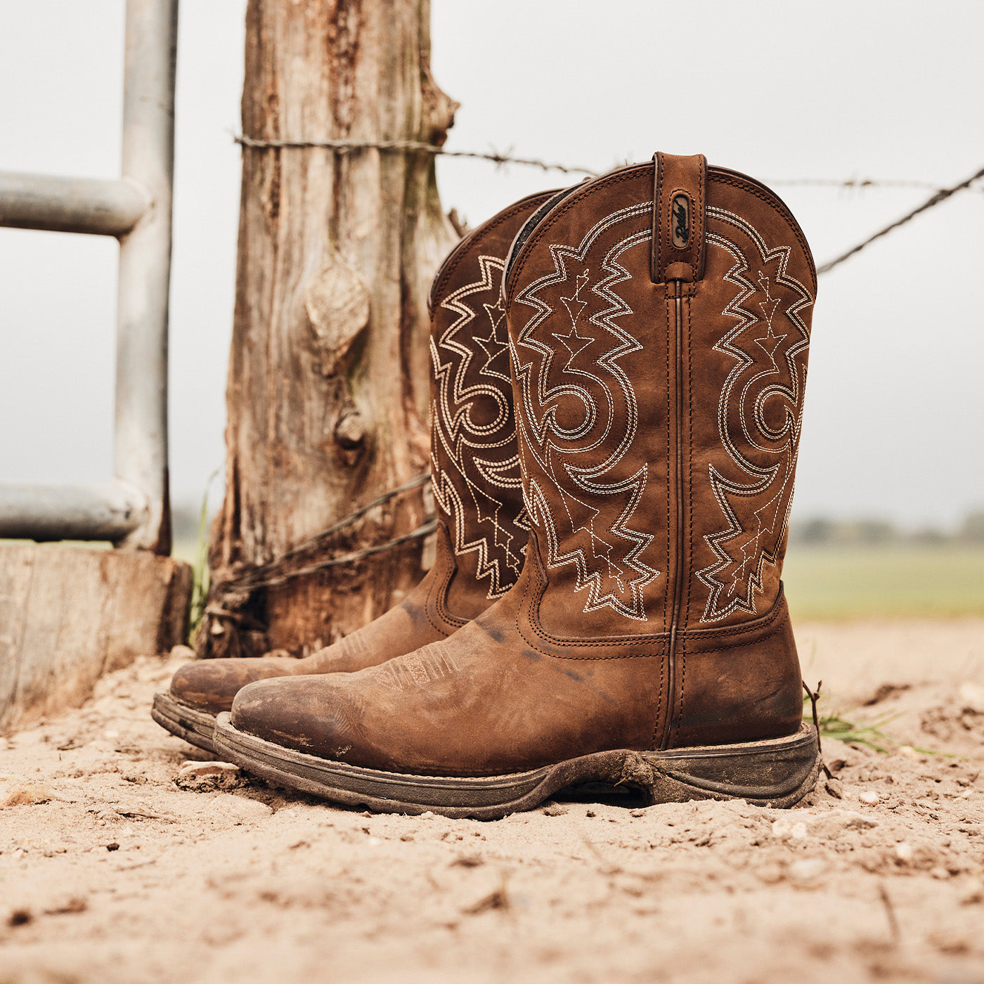 Pair of brown cowboy boots with intricate designs on a dirt ground.