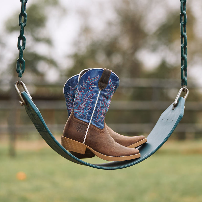 Pair of kids' Durango Shyloh cowboy boots on a playground swing with a blurred outdoor background