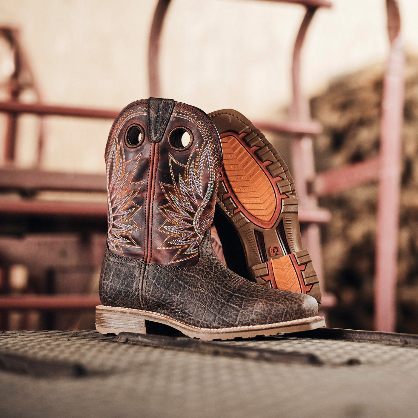 Pair of brown western work boots with elephant embossing and red leather shaft on a galvanized metal surface at a farm.