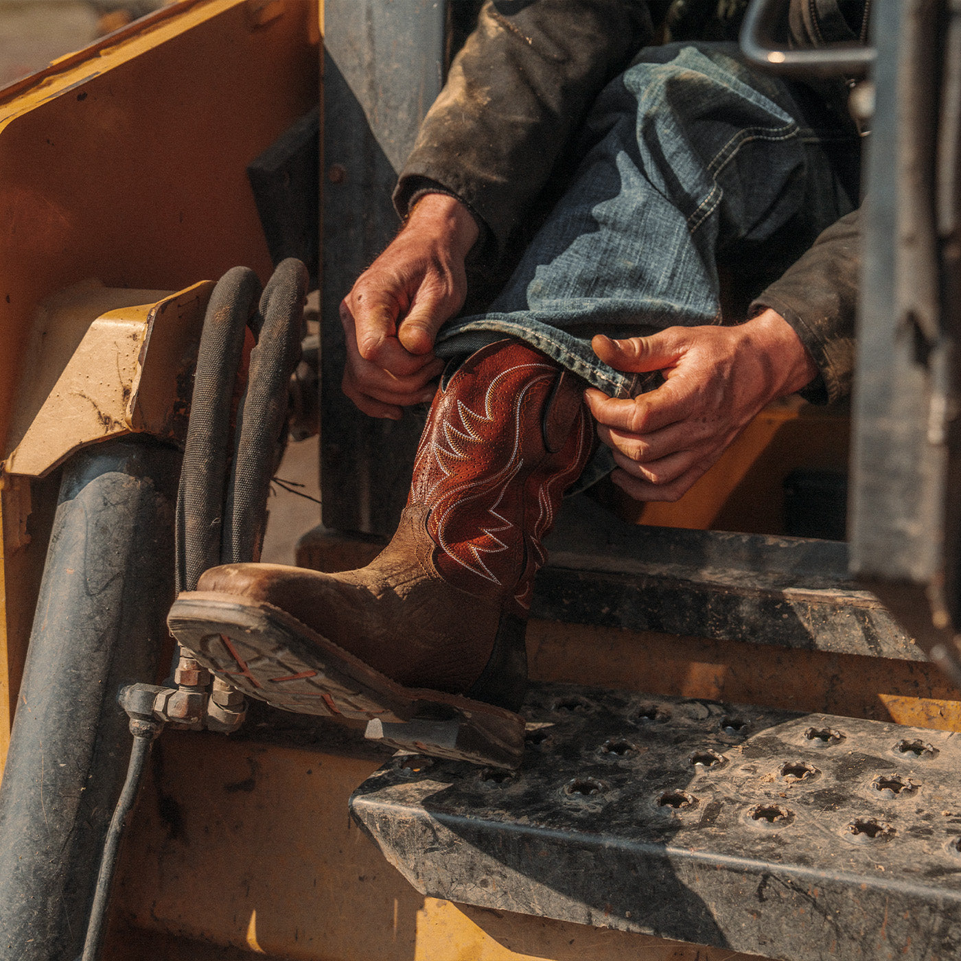 Person wearing a brown leather western work boot with red shaft color on a construction machine. 