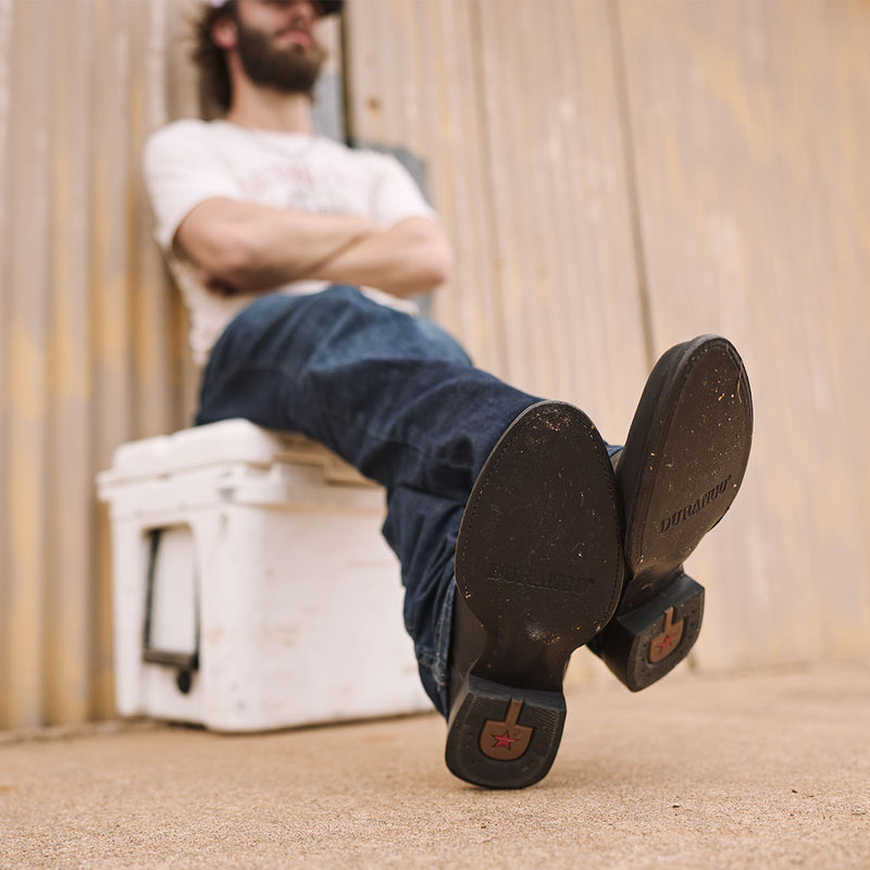 Person sitting in a cooler with feet up wearing black Durango roper boots with leather sole.