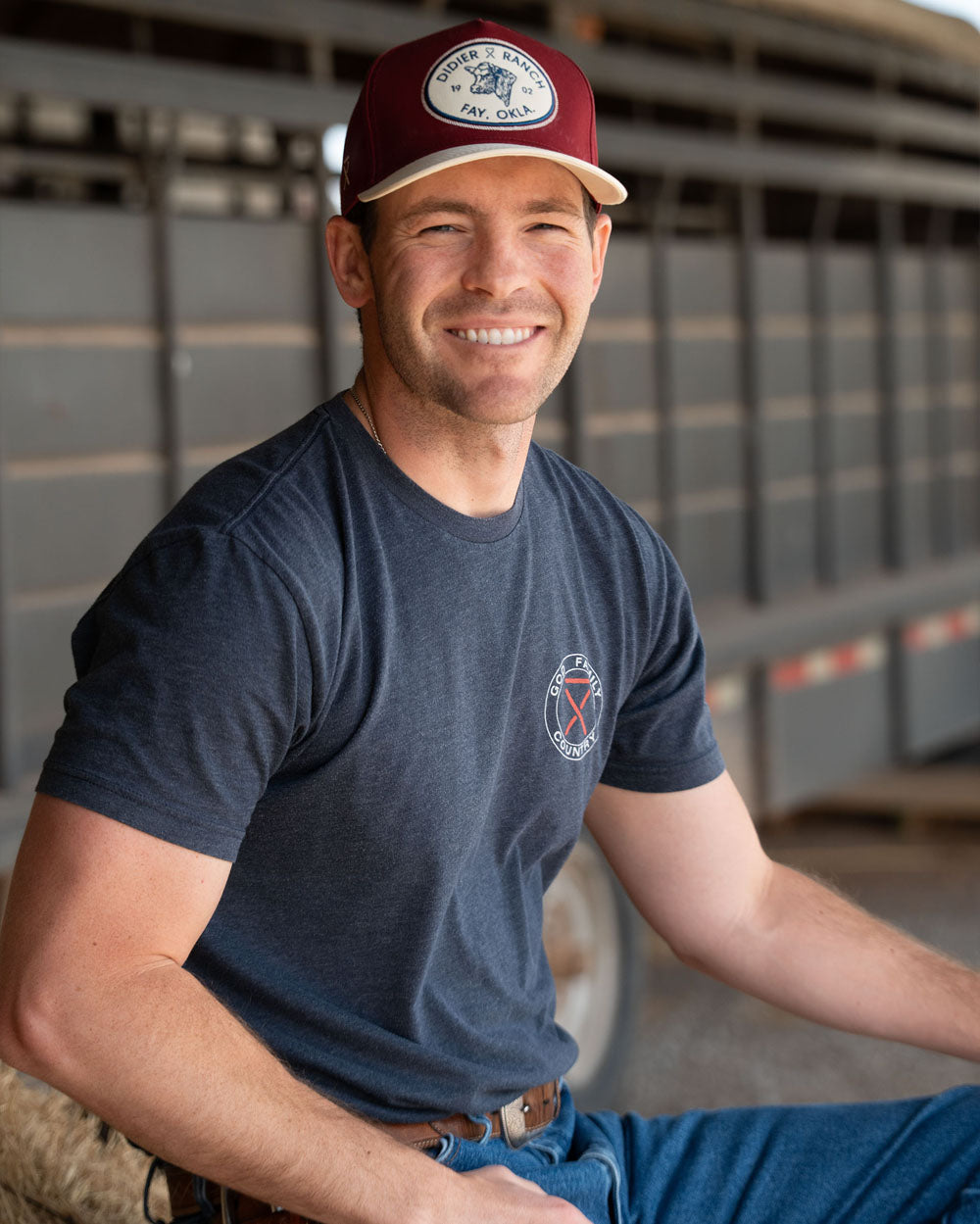Gatlin Dider wearing a navy t-shirt and red baseball cap with a logo, sitting in front of a truck.