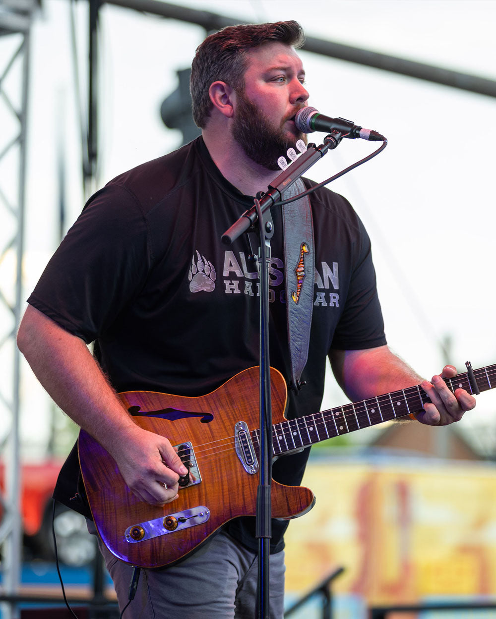 Matt Rogers playing guitar and singing into a microphone on stage.