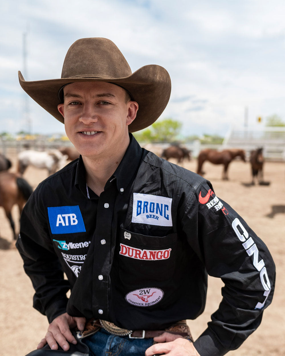 Zeke Thurston wearing a cowboy hat and a jacket with multiple brand logos in an outdoor setting with horses.
